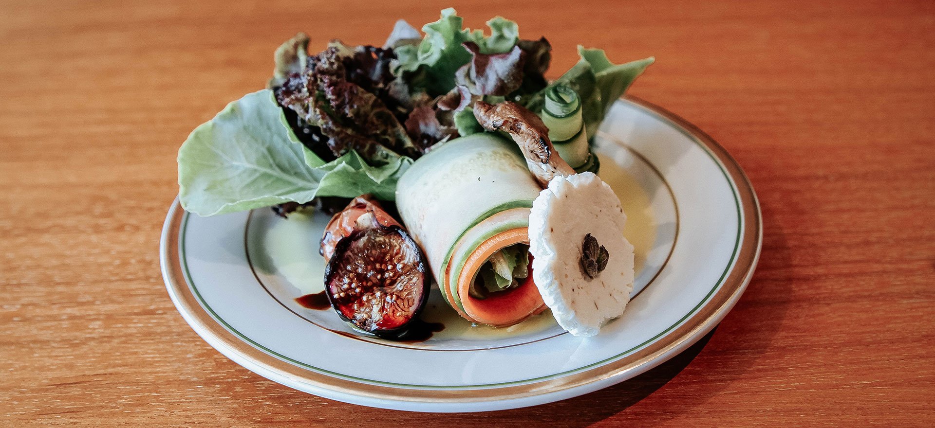 Artisan-styled catering dish featuring leafy greens, goat cheese, rolled zucchini and figs.